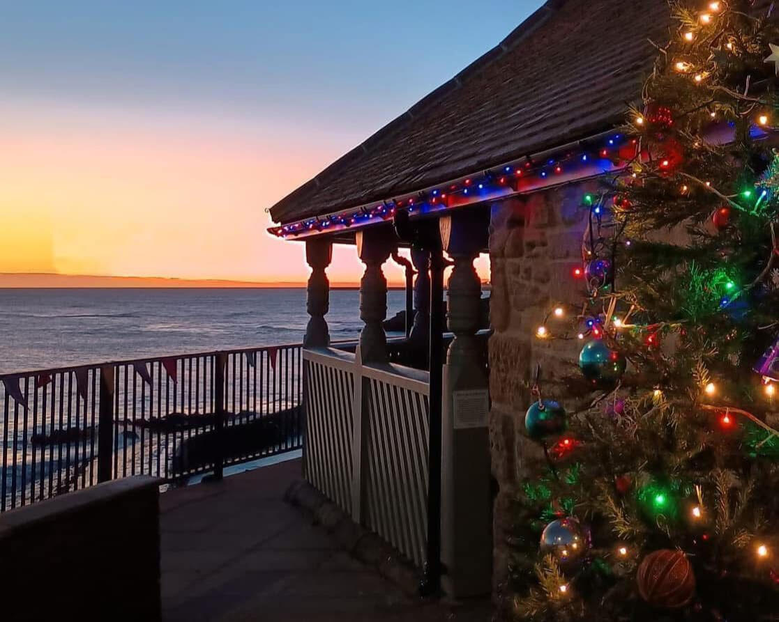 A view of the ocean from the Watch House's veranda just as the sun is setting. Christmas tree lights shine in the foreground.